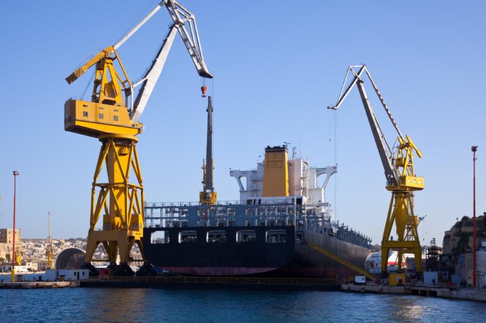 Imagen de un buque atracado siendo atendido con dos grúas amarillas.